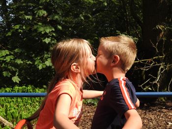 Siblings kissing while standing by railing against plants