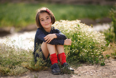 Portrait of girl holding flowers while sitting on field