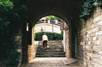 Rear view of woman moving up steps seen through archway