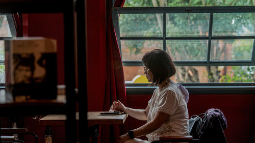 Side view of young woman sitting on window