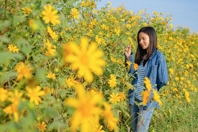 Young woman standing by yellow flowers on field