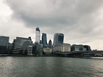 Modern buildings by river against sky in city