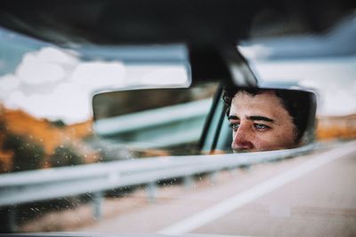 Reflection of man in rear-view mirror of car