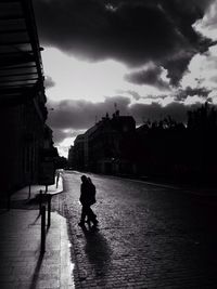 People walking in city against cloudy sky