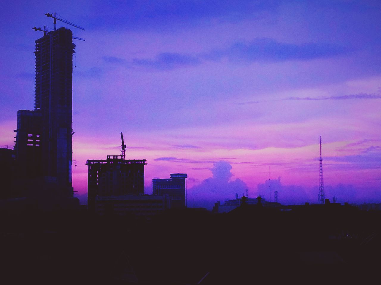 sunset, building exterior, silhouette, architecture, built structure, sky, city, orange color, dusk, low angle view, development, cloud - sky, tower, tall - high, electricity pylon, building, power line, outdoors, no people, skyscraper