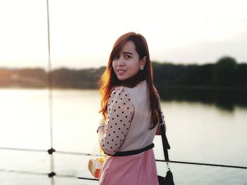 Rear view portrait of young woman standing against lake during sunset