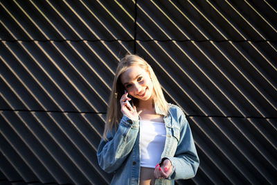 Portrait of smiling woman talking on mobile phone by wall