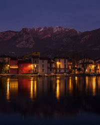 Illuminated buildings by lake against sky at dusk