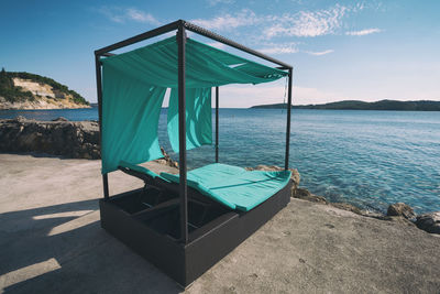 Turquoise lounge chair at sea shore in island against sky