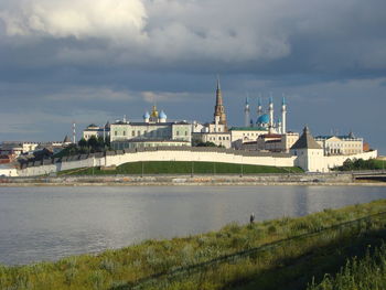 View of buildings by river against cloudy sky