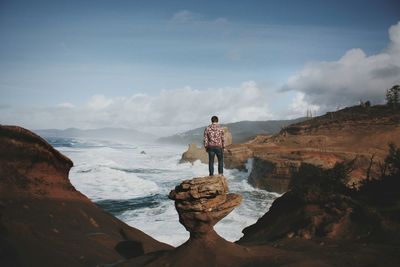 Hiker standing on rock while looking at sea amidst rock formation against sky