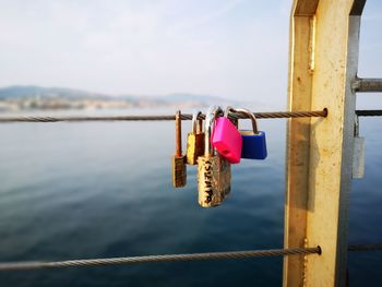 Padlocks hanging on railing by river against sky