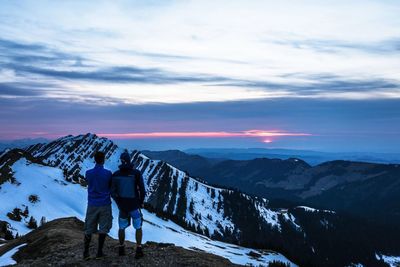 Rear view of men standing on snowcapped mountain against sky