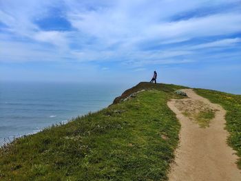 Scenic view of hiker contemplating vastness of the ocean against sky