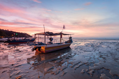 Boats moored on wet shore during sunset