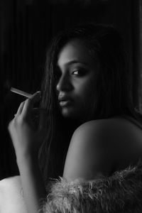 Portrait of young woman holding cigarette against black background