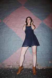 Full length portrait of young woman standing against wall