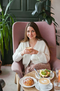 Young woman using mobile phone while sitting at restaurant having brunch