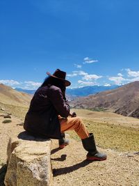 Side view of man sitting on mountain against sky