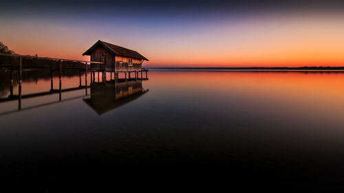 Stilt house in lake against clear sky during sunset