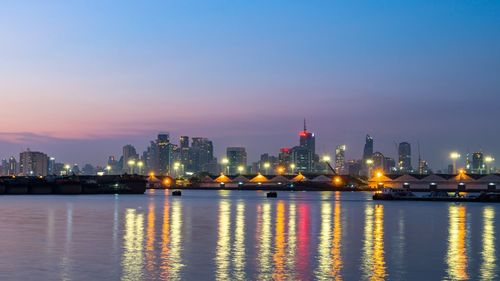 Illuminated buildings by river against sky at night