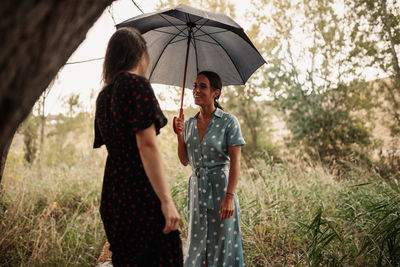 Woman talking while holding umbrella in forest