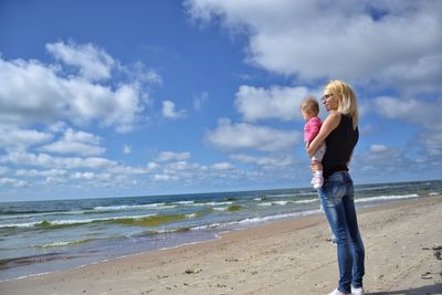 Rear view of mother holding baby girl while standing on shore at beach