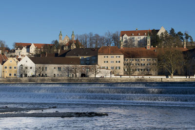 Houses by river and buildings against clear sky