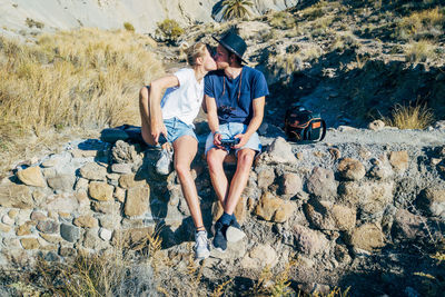 Full length of couple kissing while sitting on rocks