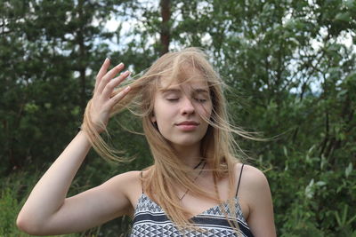 Beautiful young woman with eyes closed standing against trees in forest