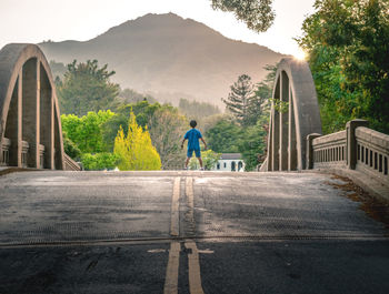 Rear view of man walking across bridge  by trees