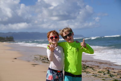 Young boy smiling with an aloha sign wearing sunglasses on the beach in hawaii. 
