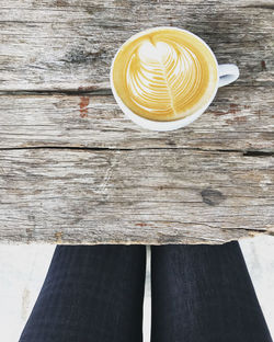 Directly above shot of cappuccino on the table with lady's legs on black pants