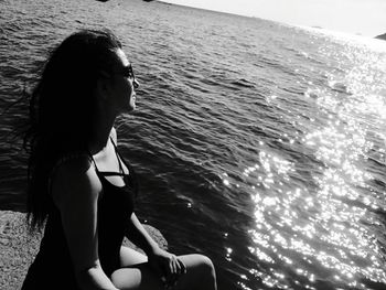 Woman sitting on jetty by sea during sunny day