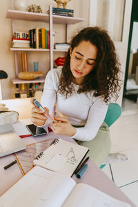 Young woman with curly hair using glucometer while doing homework at home