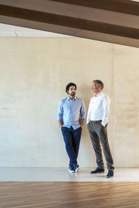 Senior businessman discussing strategy with colleague in front of wall