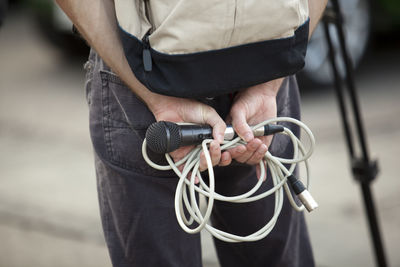 Midsection of man holding microphone standing outdoors