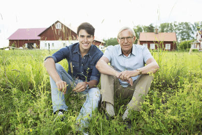 Full length portrait of grandfather and grandson sitting on grassy field