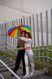 Full length of woman with umbrella standing against wall