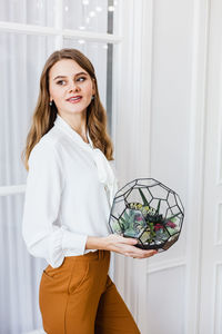 Portrait of smiling young woman standing against white wall