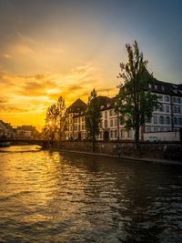 Buildings by river against sky during sunset