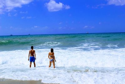 Rear view of men walking on beach against blue sky