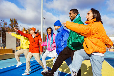 Low angle view of people with arms raised standing against sky