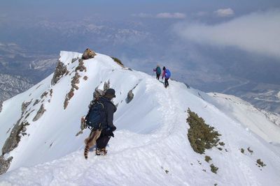 Rear view of hikers climbing on snowcapped mountain