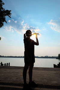 Silhouette woman drinking water while standing by lake