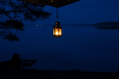 Illuminated lamp post in lake against sky at night