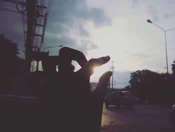 Optical illusion of cropped hand reaching electricity pylon