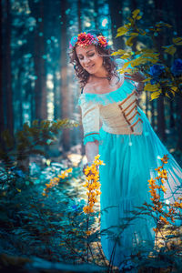 Portrait of young woman standing by tree in forest