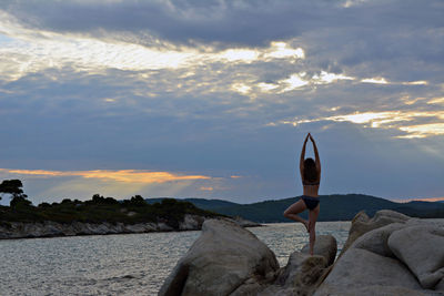 Woman on rock by sea against sky during sunset