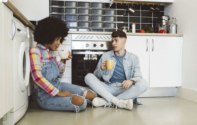 Multiracial couple having coffee together sitting in kitchen at home